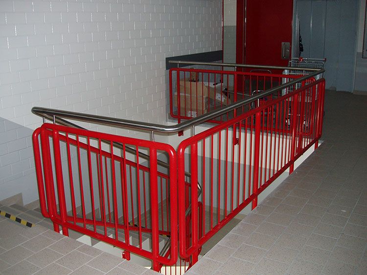 Červené zábradlí schodiště u administrativní budovy s nerezovým madlem