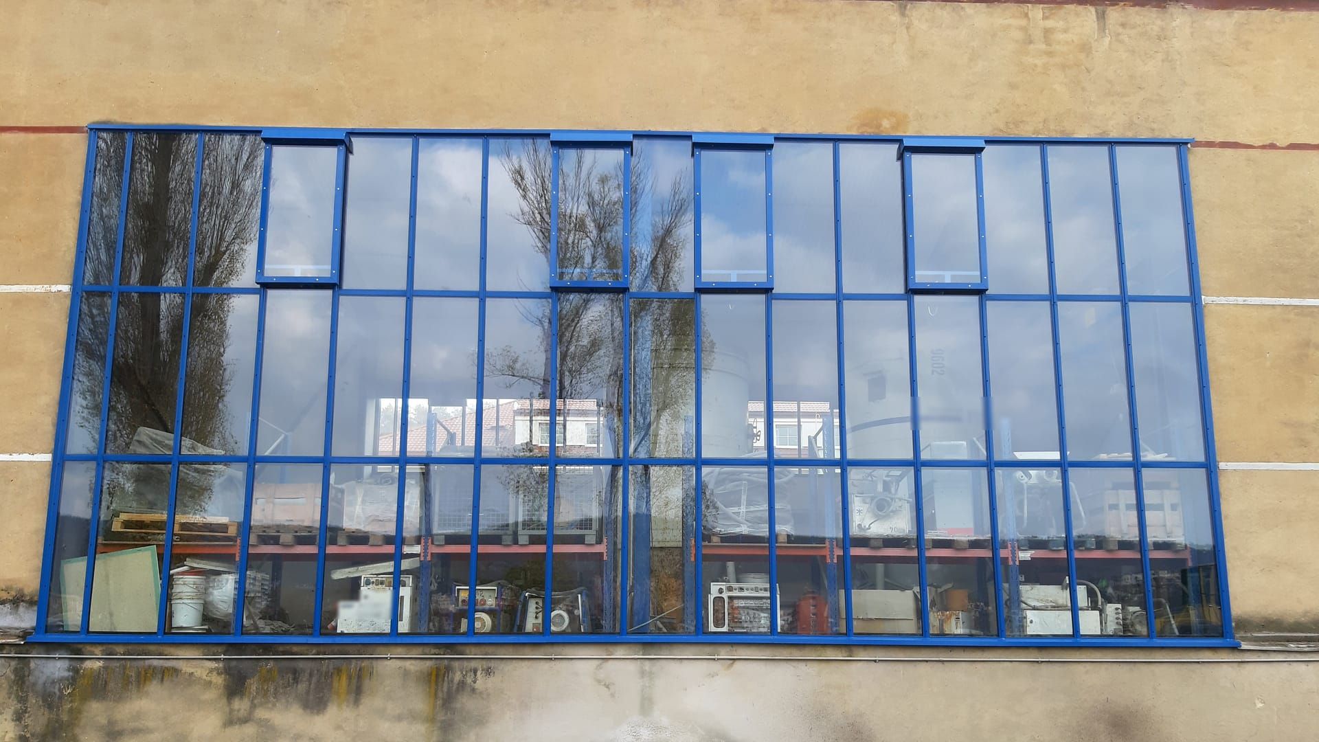 Nová prosklená stěna s modrými rámy a větracími křídly na průmyslové hale ve Středočeském kraji